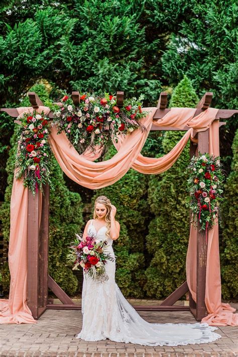 Outdoor Wedding Ceremony With Beautiful Florals And Draped Fabric On Arbor