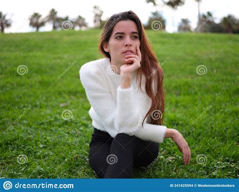 A Thoughtful Young Woman Sitting On The Grass In The Park Propping Face