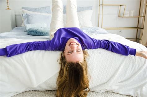Girl Lies On The Bed Upside Down In Purple Sweater And Smiles At The Camera Concept Morning And