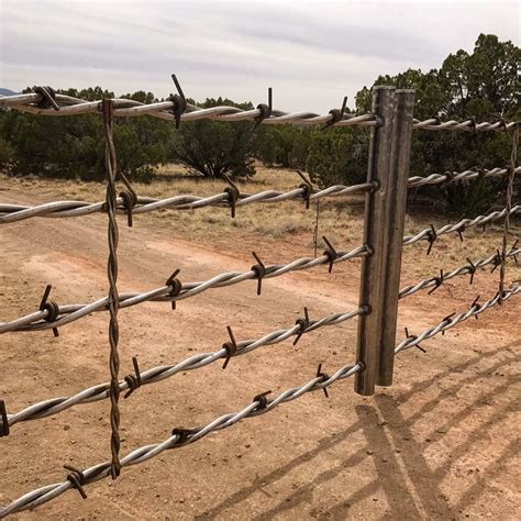 A Fence With Barbed Wire In The Middle Of A Dirt Field