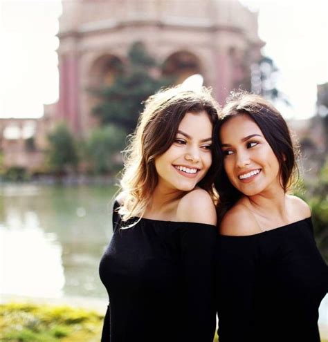 two beautiful women standing next to each other in front of a lake with trees and bushes