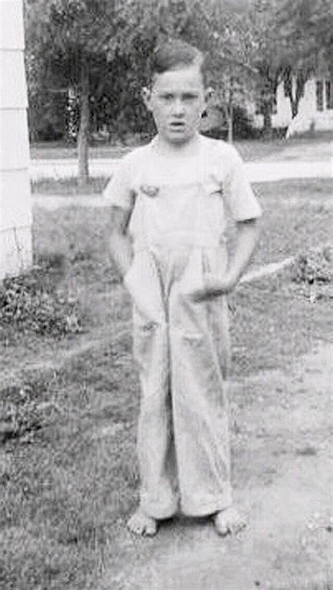 An Old Black And White Photo Of A Young Boy In Overalls Standing On The
