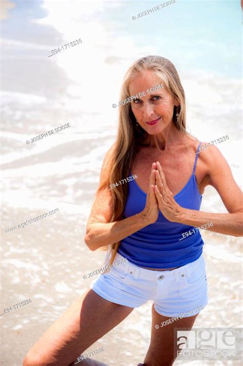 Portrait Of A 57 Year Old Woman On A Beach Smiling At The Camera Hands In Prayer Pose Stock