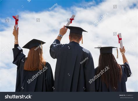 Portrait Of Happy Students In Graduation Gowns Holding Diplomas On