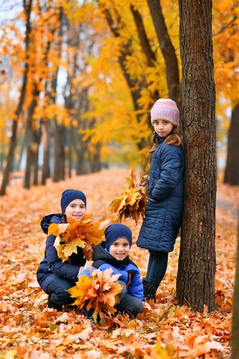 Children Playing With Yellow Maple Leaves In Autumn City Park They Are