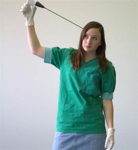 A Woman In Scrubs Holding A Microphone Up To The Side With One Hand And Two Other Hands Behind