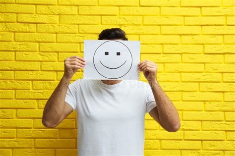 Man Hiding Emotions Using Card With Drawn Smiling Face On Beige