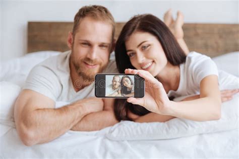 Portrait Of Newly Married Couple Taking Selfie In Bed Stock Image