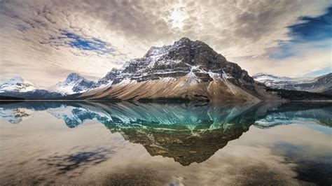 Snow Capped Mountain Reflection On Calm Water Under Cloudy Sky