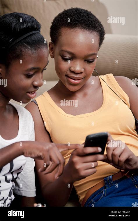 Two African Teenage Girls Sit Together In A Lounge Looking At Their Cellphones Stock Photo Alamy