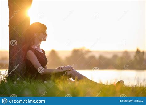 Lonely Woman Sitting Alone On Green Grass Lawn Leaning To Tree Trunk On