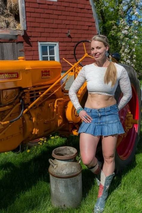 A Woman Standing Next To A Tractor In The Grass With Her Hands On Her Hips