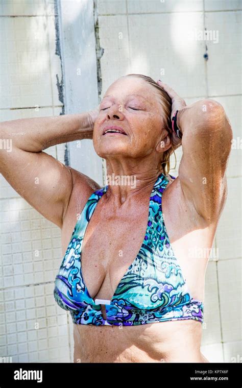 Older Retired Senior Caucasian Woman Showering At The Beach In A Blue Bathing Suit Stock Photo