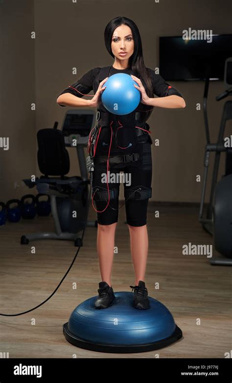 Brunette Girl In Electrical Muscular Stimulation Suit Stands On Bosu