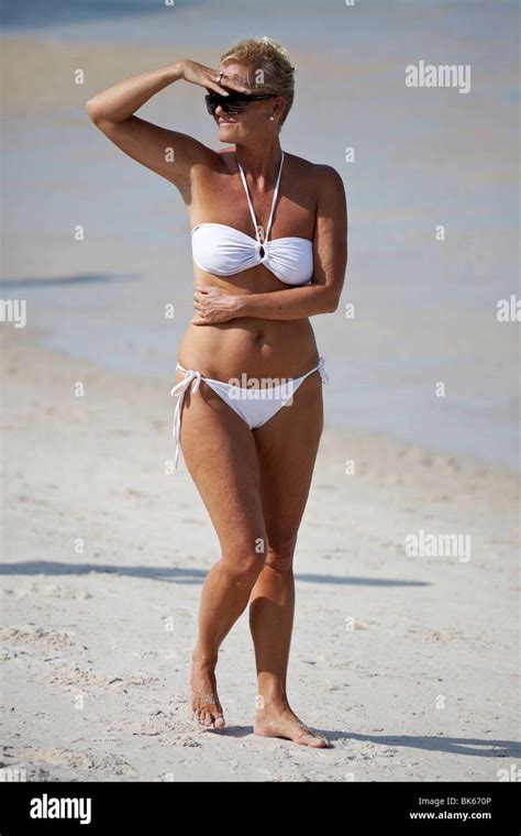 gesund und fit aussehende reife frau in einem weißen bikini allein an einem tropischen strand s