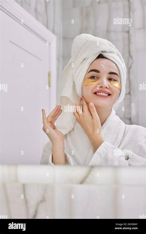 Beautiful Woman With Eye Patches In White Bathrobes Massaging Face In