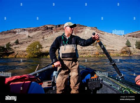 A Fisherman Guides A Dory Boat On The Deschutes River With Mountains In