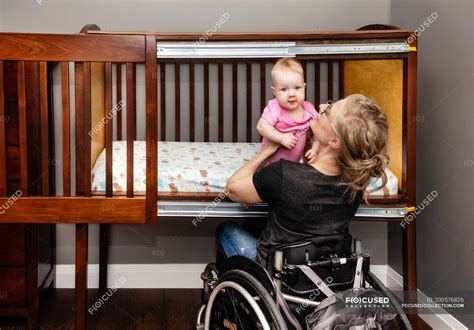 A Paraplegic Mother Lifting A Baby From A Customized Side Opening Crib