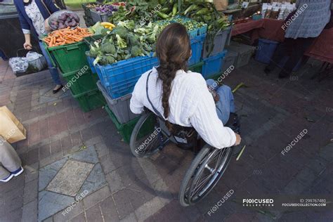 Woman With Spinal Cord Injury In Wheelchair Shopping At Outdoor Market