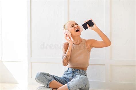 Joyful Woman Wearing Wireless Headphones And Using Cellphone As Mic Singing While Sitting On