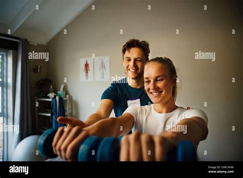 Male Physiotherapist Observing Female Patient Holing Weights Stock