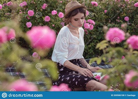 Beautiful Girl Wearing Hat With Book Sitting On Grass In Rose Gaden