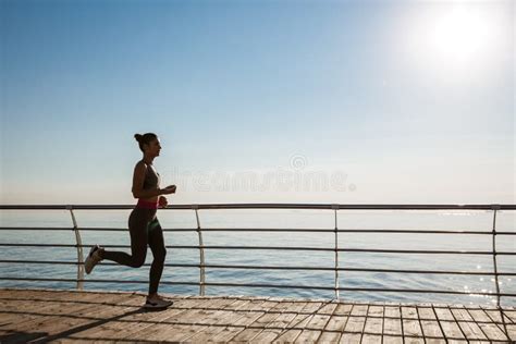 Side View Of Young Fitness Woman Running Along Pier Female Athlete