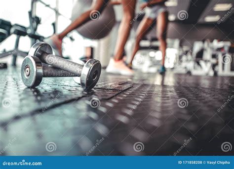 Dumbbell On A Flor In Fitness Gym With Legs In Background Stock Photo
