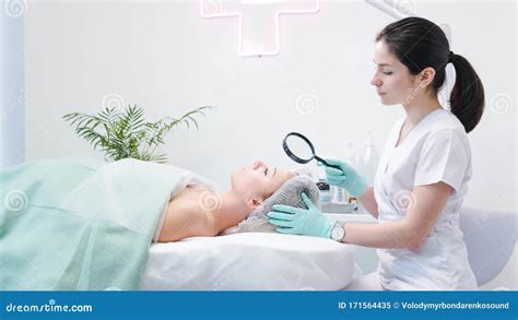 The Female Dermatologist Examining Face Of Young Patient With