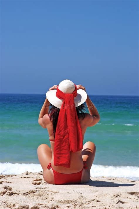 Frau Im Roten Bikini Der Auf Dem Strand Justiert Hut Sitzt Stockfoto