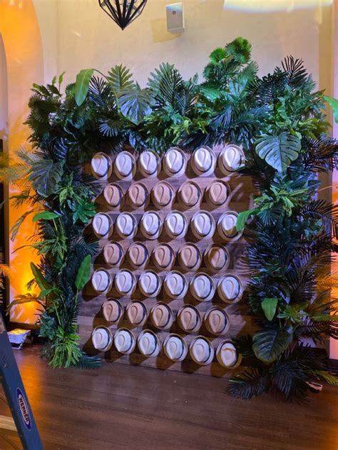 Havana Nights Inspired Backdrop With Tropical Greenery And Fedora Hats For A Corporate Holiday