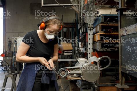 Young Australian Female Tradesperson Using Belt Sander In Metal