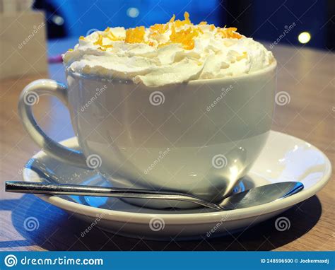 A Cup Of Cappuccino With Whipped Cream Sprinkled With Orange Zest Is On