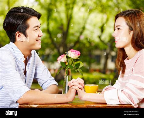 Young Asian Man And Woman Sitting Face To Face Holding Hands Looking At