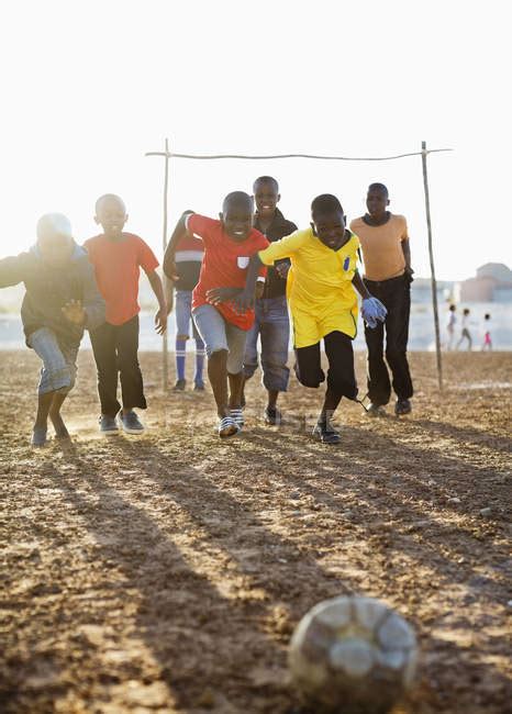 African Boys Playing Soccer Together In Dirt Field — Happiness Casual