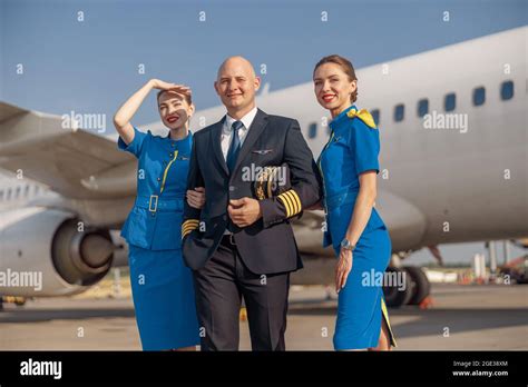 Happy Pilot And Two Attractive Stewardesses Standing Together In Front