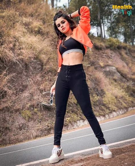 A Woman Standing On The Side Of A Road Wearing Black Pants And An Orange Jacket