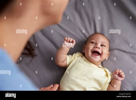 Mother Playing With Newborn Baby Son Lying On Bed In Nursery Stock