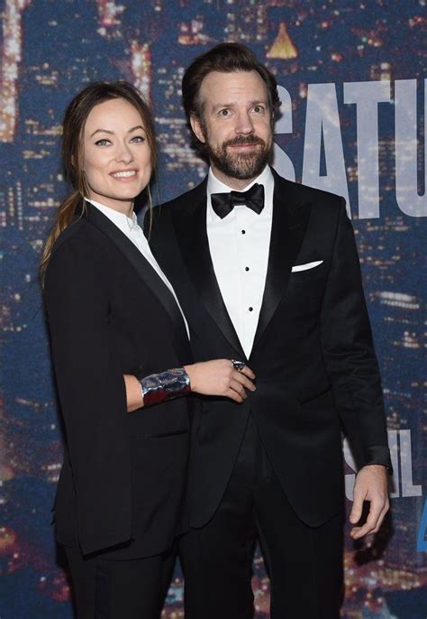 A Man And Woman In Tuxedos Standing Next To Each Other On A Red Carpet