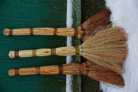 Three Brooms In The Snow Near The Green Wooden Wall Stock Photo