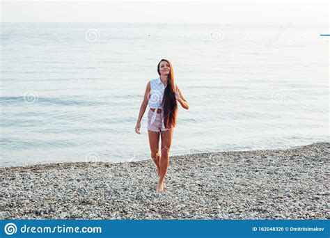 Beautiful Tanned Woman With Long Hair Walks On The Beach By The Sea