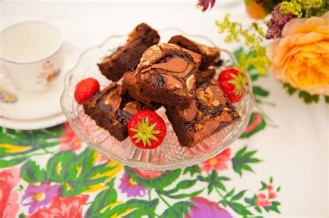Some Brownies And Strawberries In A Glass Bowl On A Floral Tablecloth