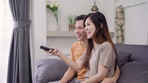 Asian Couple Watching Tv And Drinking Warm Cup Of Coffee In Living Room