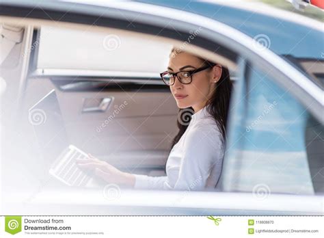 Young Woman In Glasses Sitting In A Backseat Of A Car With Laptop And