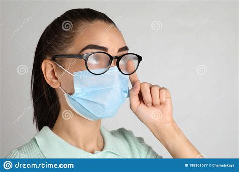 Woman Wiping Foggy Glasses Caused By Wearing Medical Mask On Light Background Stock Image