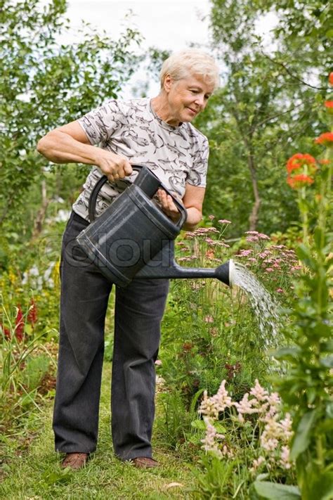 Die ältere Frau Gießt Wasser Auf Blumen Im Garten Im