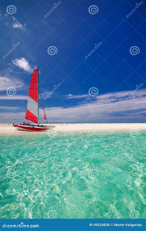 Sailing Boat With Red Sail On Beach Of Tropical Island Stock Photo