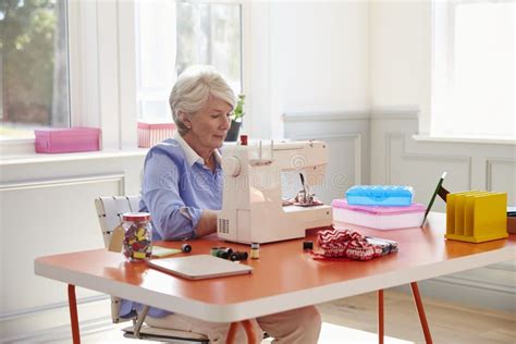 Senior Woman Making Clothes Using Sewing Machine At Home Stock Photo