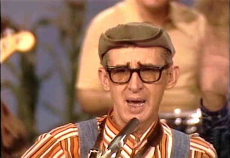 A Man Wearing Glasses And A Hat Is Holding A Microphone In Front Of His