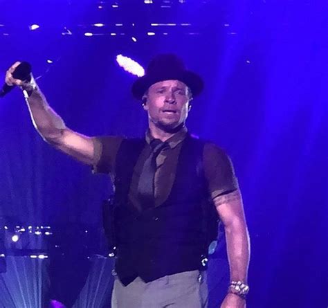 A Man Wearing A Hat And Vest Holding A Microphone In His Right Hand